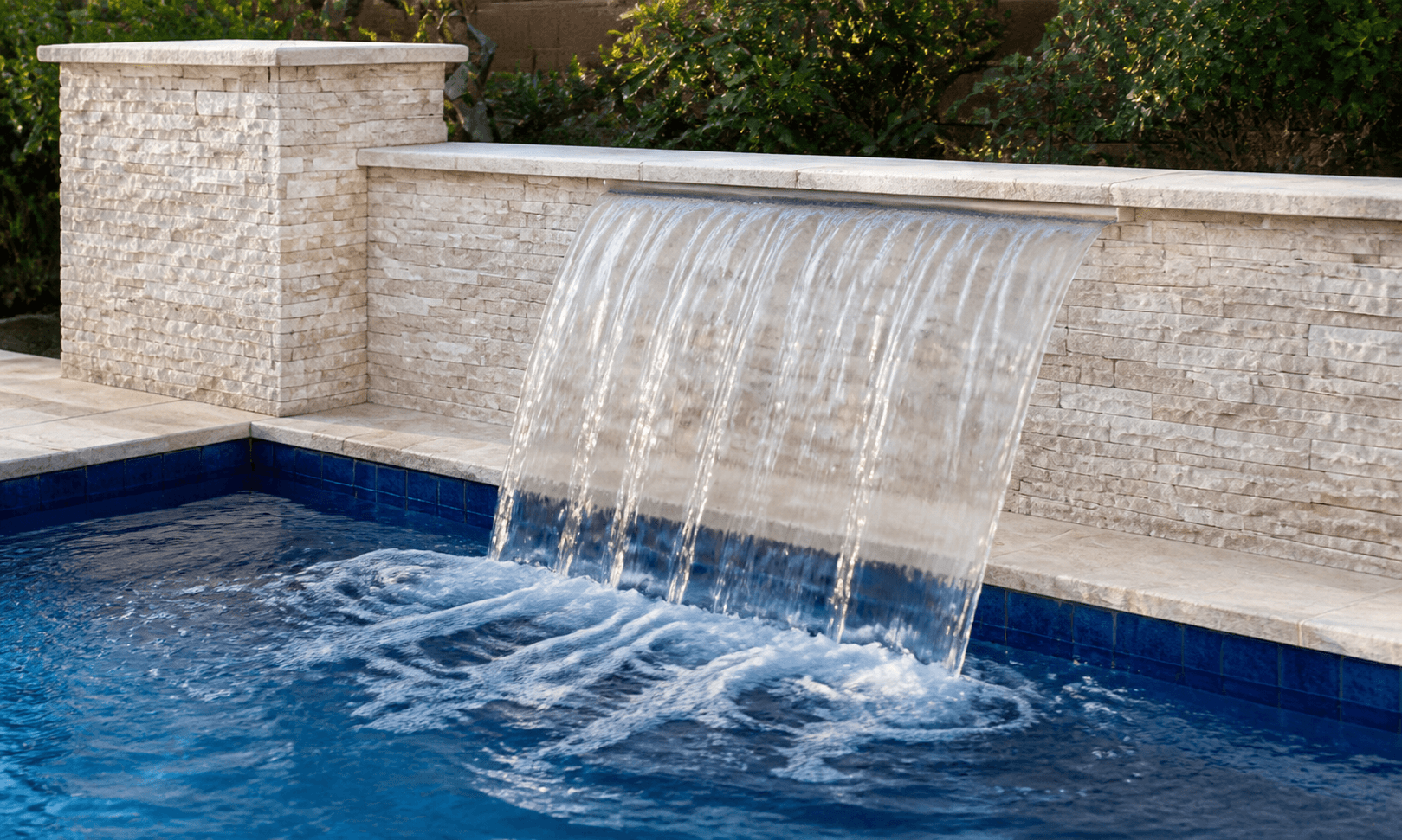 Wide sheet waterfall flowing from a stacked-stone pool wall