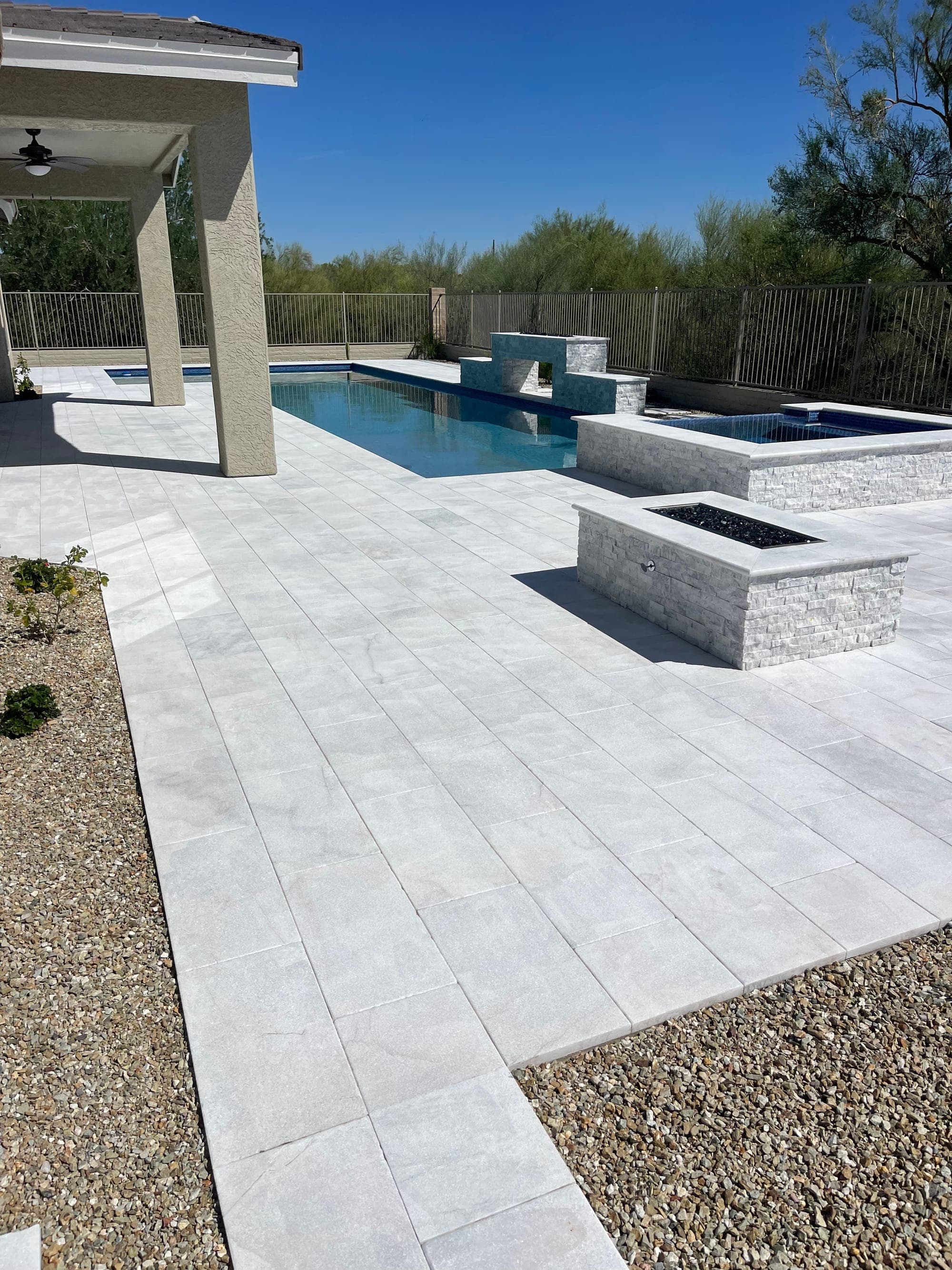 Light concrete-paver pool deck with a stacked-stone fire pit and raised spa under a covered patio