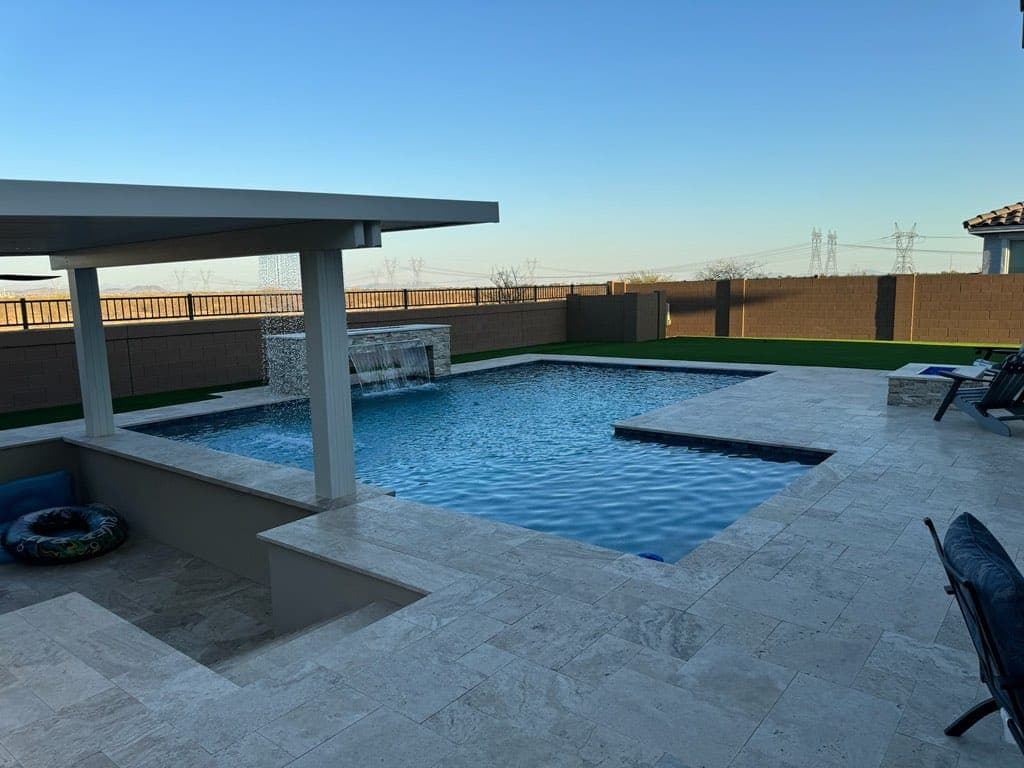 White pergola over travertine decking beside a pool with a sheer descent from a raised wall
