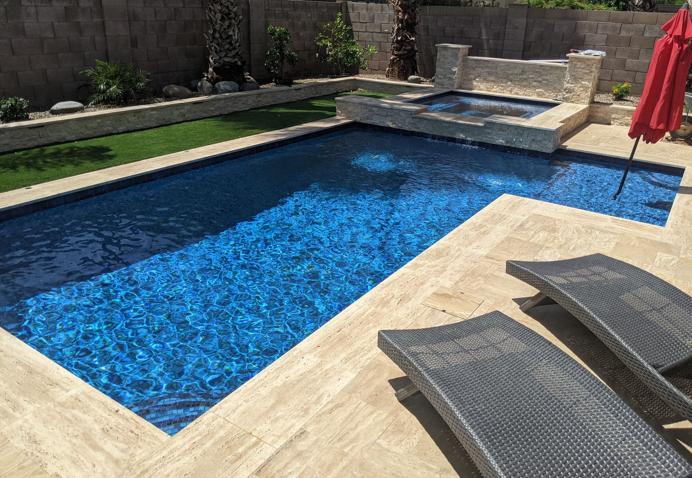 Modern Pools custom pool with travertine deck, lounge chairs, and raised spa wall in an Arizona backyard