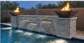 Stacked stone waterfall feature spilling into a pool with desert mountains beyond
